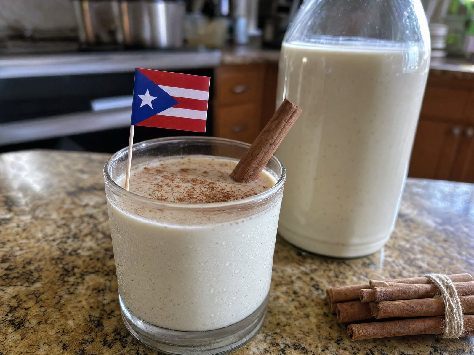A small glass of creamy white coquito dusted with cinnamon and garnished with a cinnamon stick, next to a glass bottle of coquito