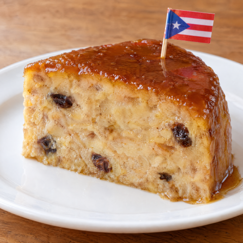 Slice of Puerto Rican budín de pan with raisins and golden caramel on a white plate