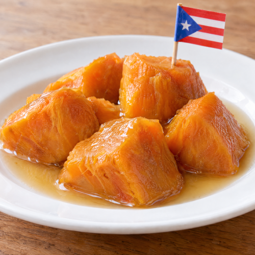 Orange sweet-potato pieces in cinnamon-vanilla syrup served on a white plate as dulce de batata en almíbar