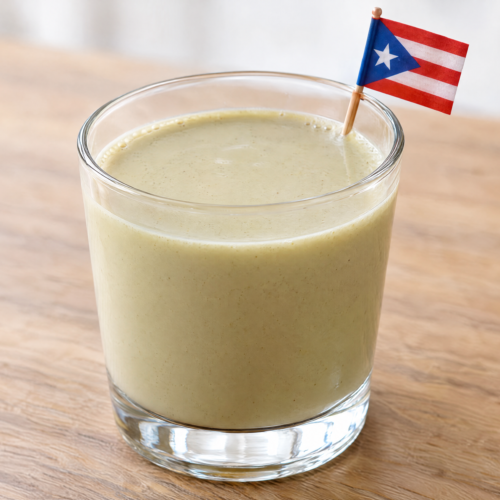 Creamy pale-green coquito de pistacho in a small clear glass on a natural wooden table