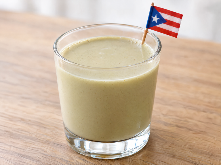 Creamy pale-green coquito de pistacho in a small clear glass on a natural wooden table